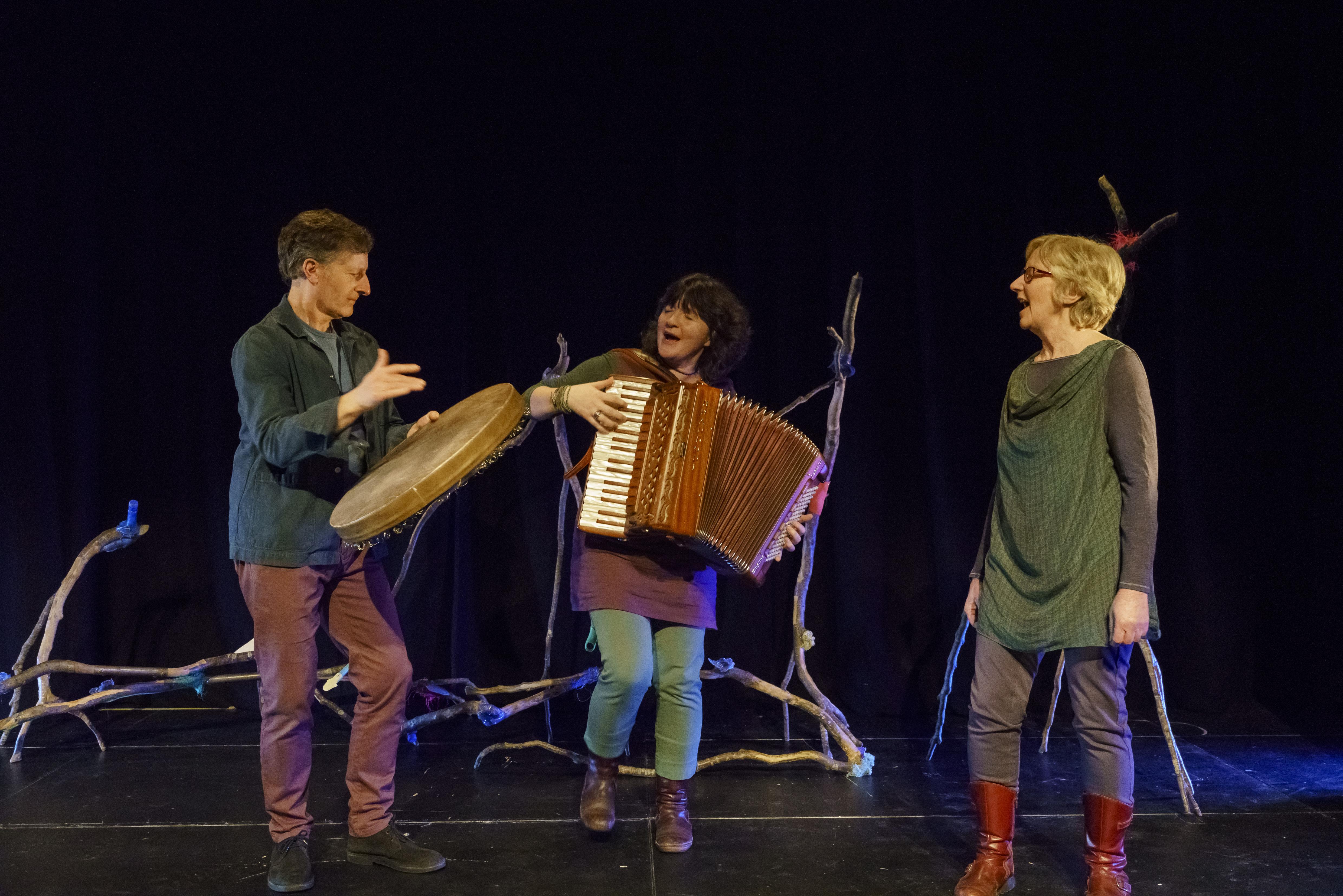 three artists on stage, (l-r) Michael Harvey plays the bodhran, Stacey Blythe plays the accordion and Lynne Denman sings