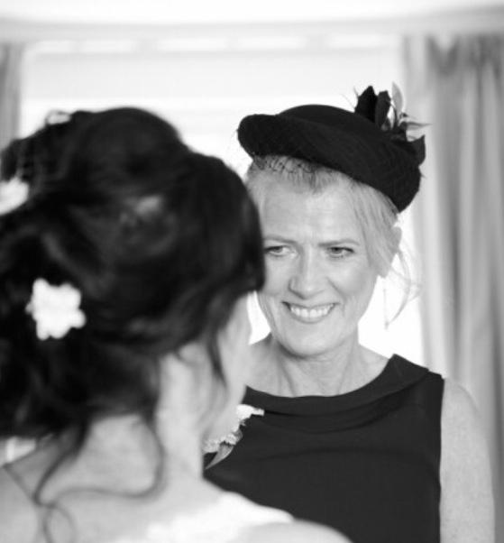 A woman with blond hair tied back, wearing a black dress and hat. This photograph shows her at her daughter's wedding