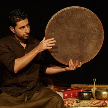 Arash Moradi on stage wearing a dark shirt and playing the drum, the tanbour
