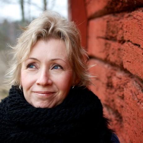 A white woman with blond hair wearing a high necked black coat