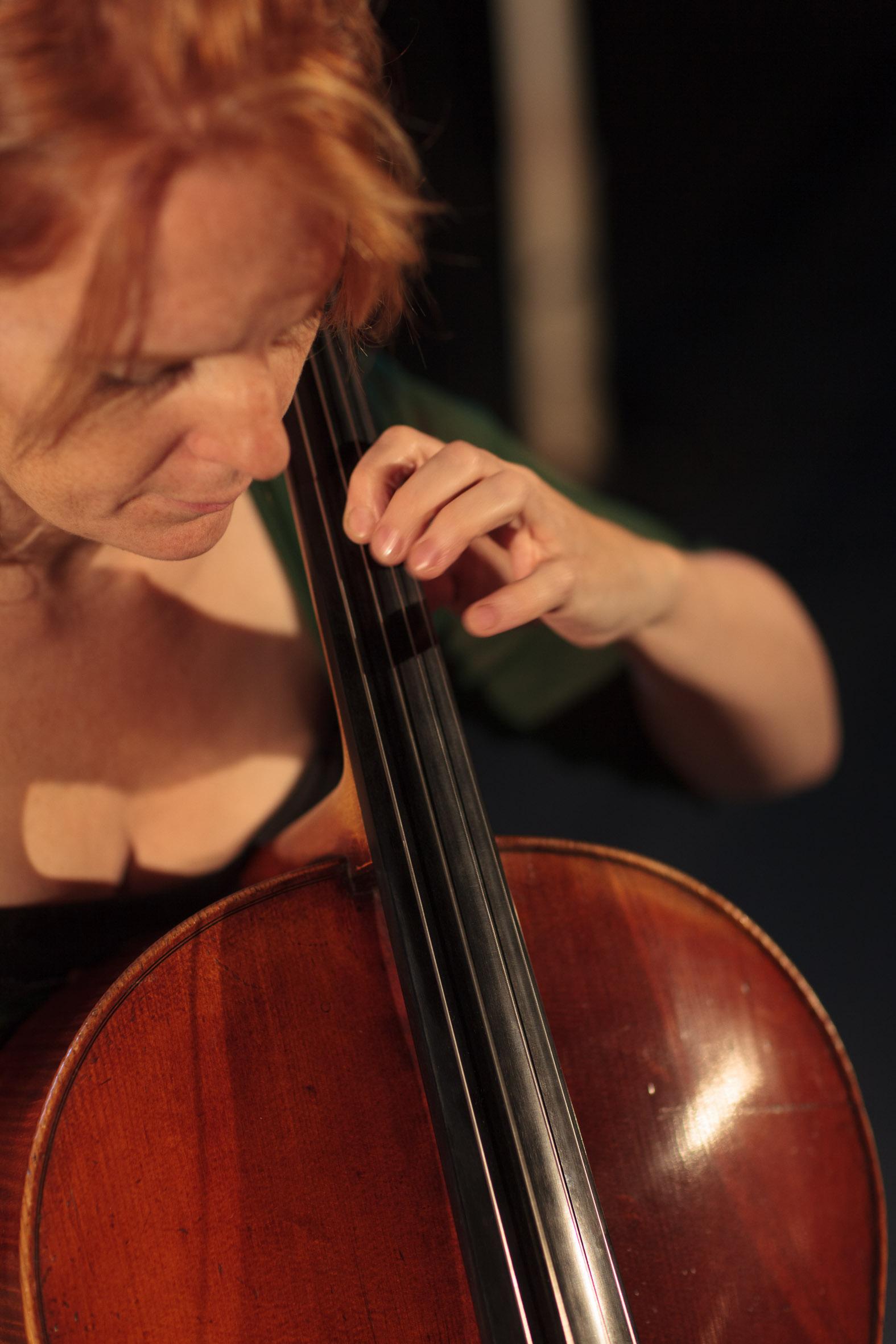 a young white woman with red hair tied back at the sides, wearing a green dress and playing the cello
