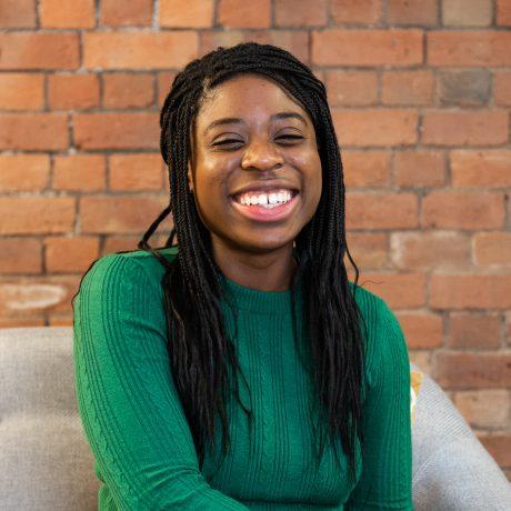 a young black woman with long dark hair and wearing a green jumper