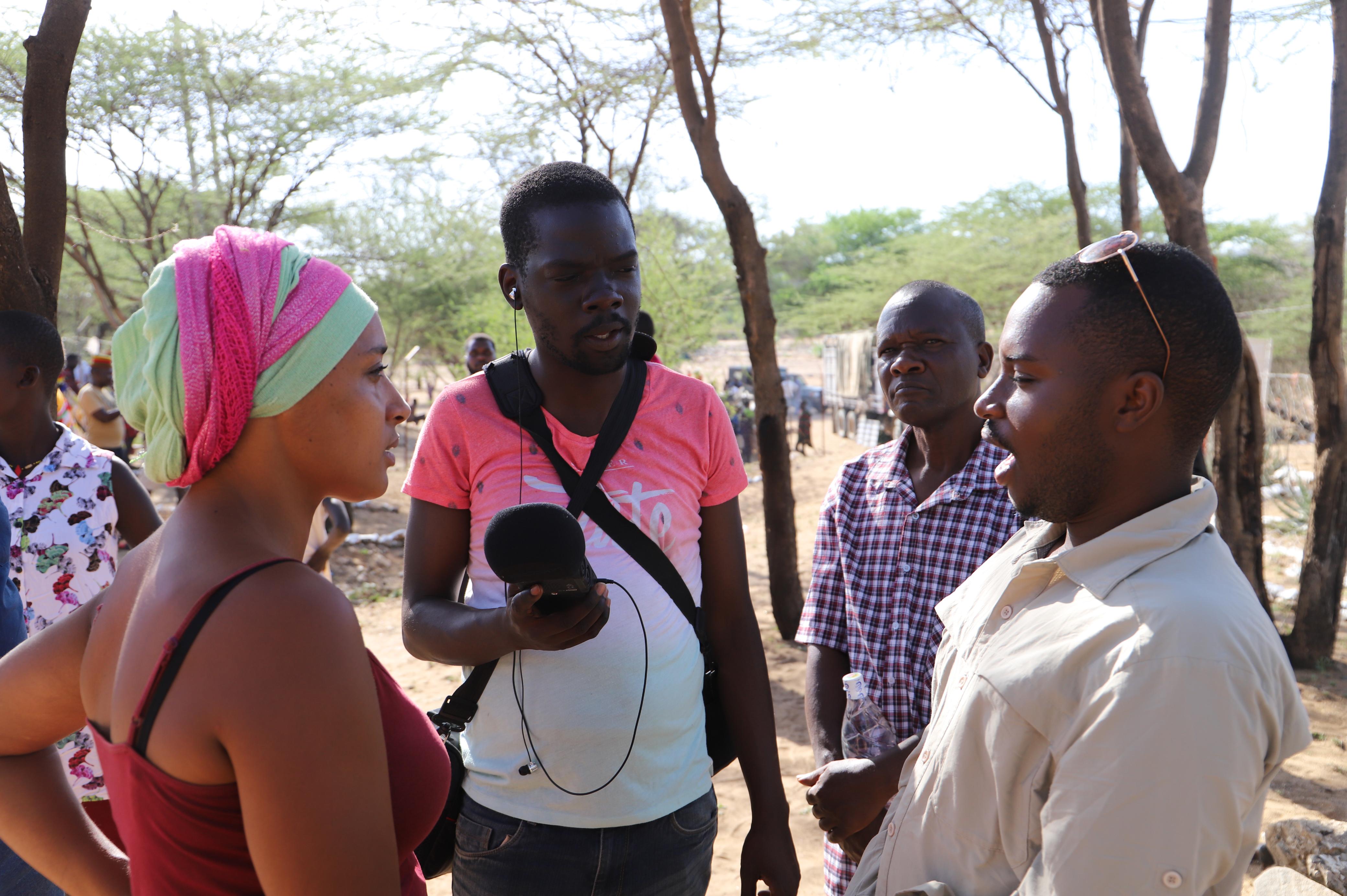 From Left: Storytellers Mara Menzies and John Namai interview Obed Tuyumvire, an entrepreneur (right) at the Lokiriama Peace Accord Commemoration in Lokiriama village, Turkana County, Kenya. Looking on is Turkana County Meteorological Services Director Francis Muinda.