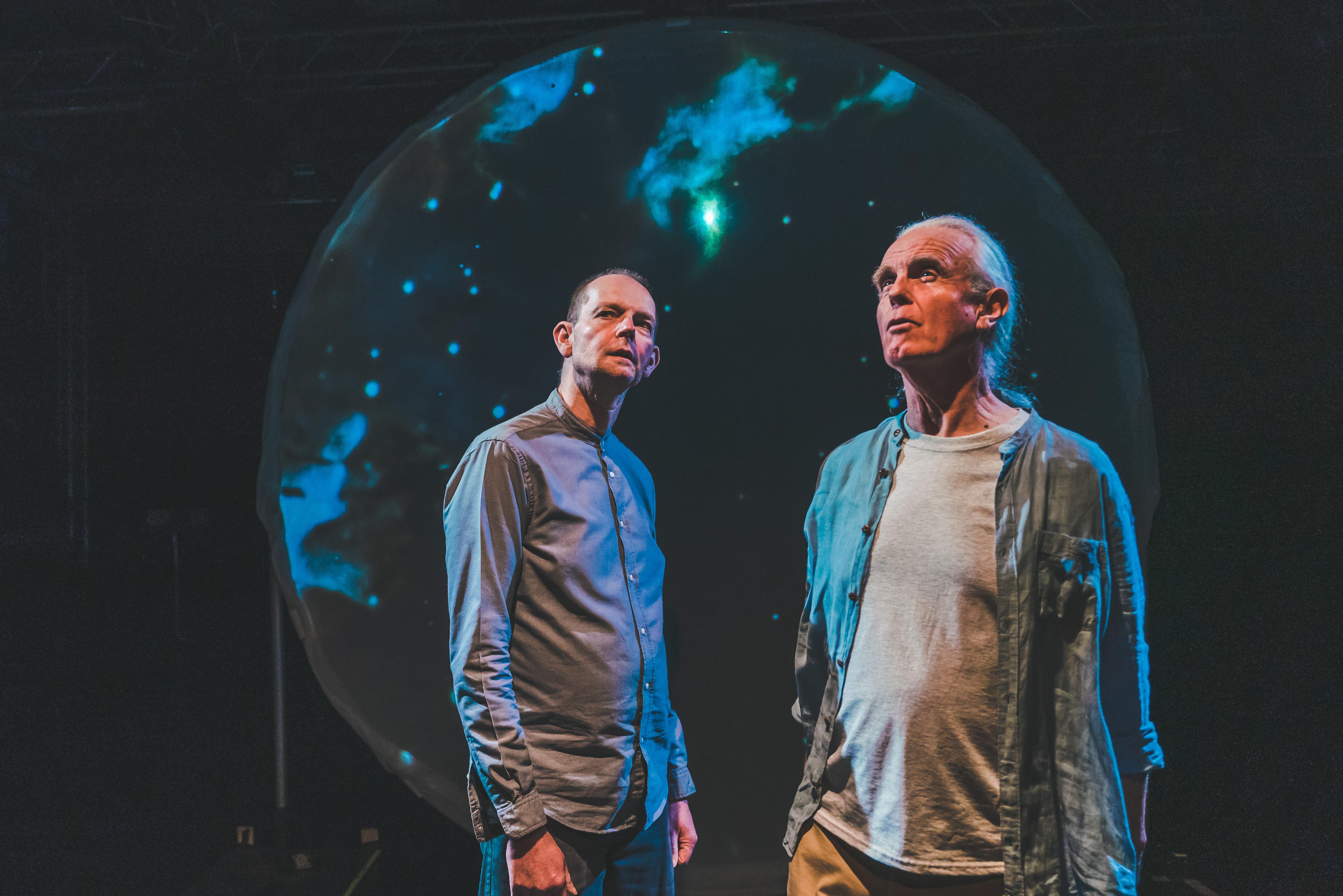 Daniel Morden and Hugh Lupton stand in front of a large disc covered in cosmic projections