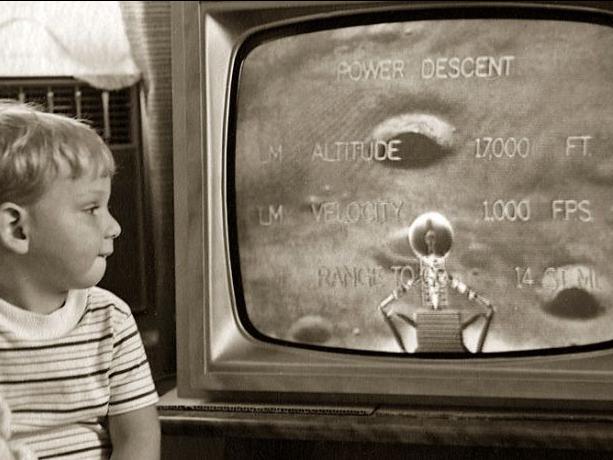 a black and white photo of a young child looking at the television showing a close up of the moon's surface