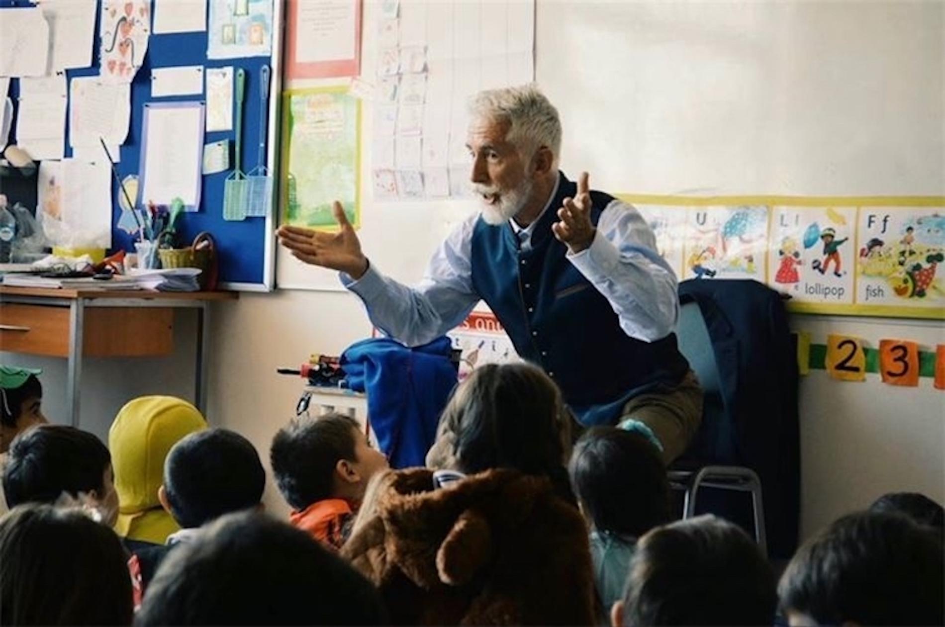 Sef Townsend, a man with white hair and beard tells stories to a group of young people sitting on the floor