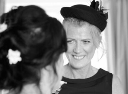 A woman with blond hair tied back, wearing a black dress and hat. This photograph shows her at her daughter's wedding