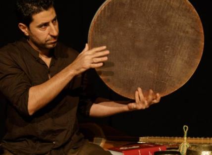 Arash Moradi on stage wearing a dark shirt and playing the drum, the tanbour