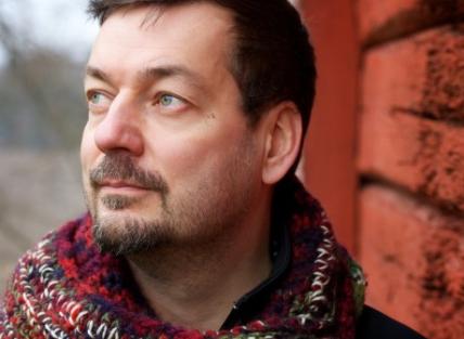 A white man with short dark hair and a beard, wearing a multi coloured scarf