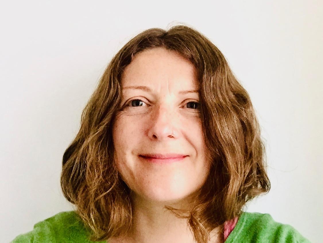 A woman with shoulder length light brown hair, wearing a green jumper