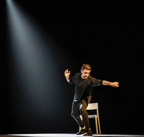 Lewis Doherty on stage with a chair and a beam of light