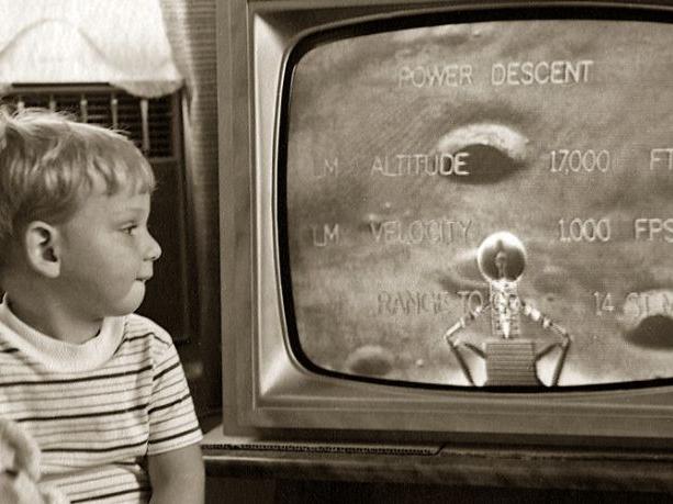a black and white photo of a young child looking at the television showing a close up of the moon's surface
