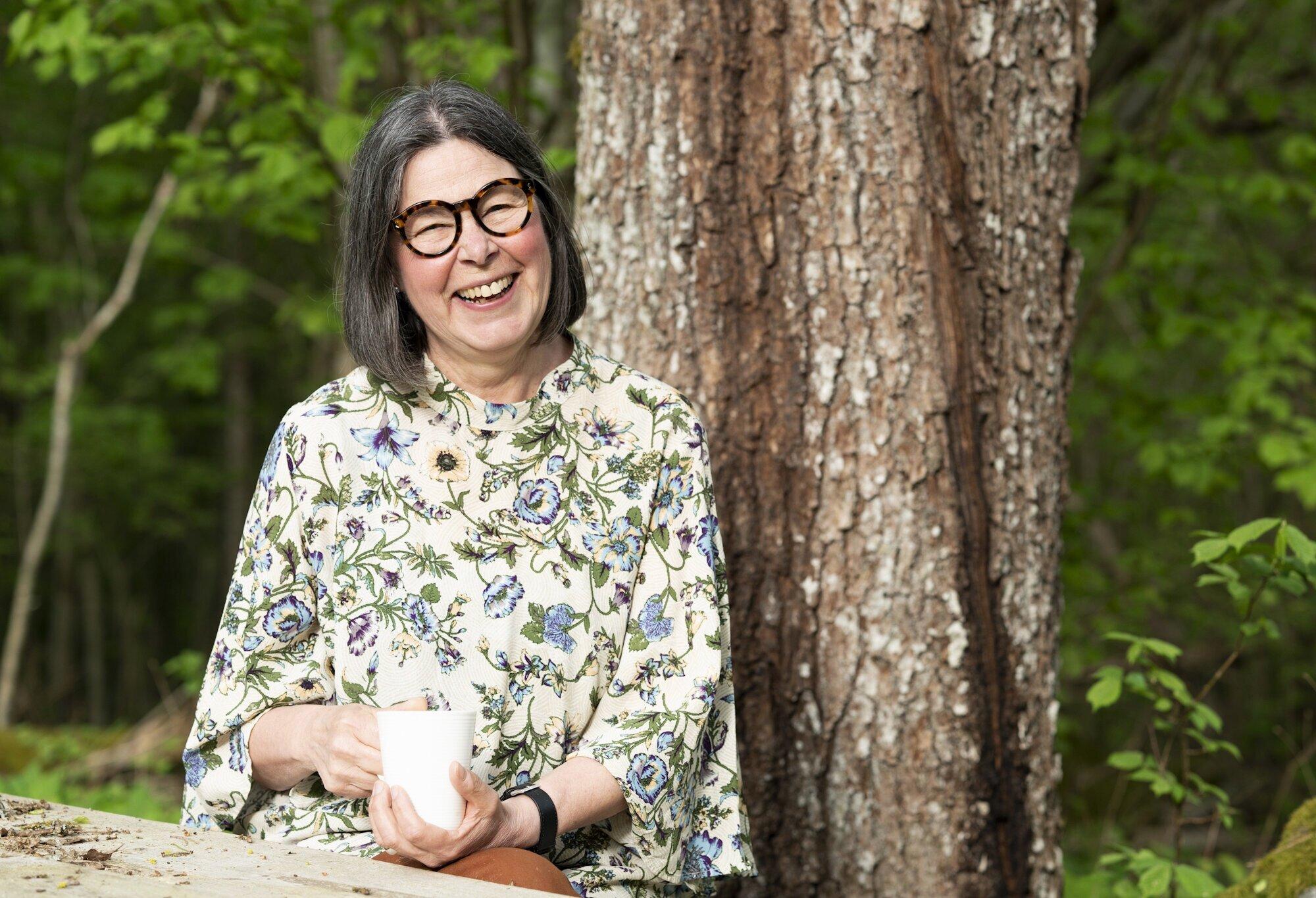 a white woman with shoulder length dark hair, wearing glasses and a floral shirt