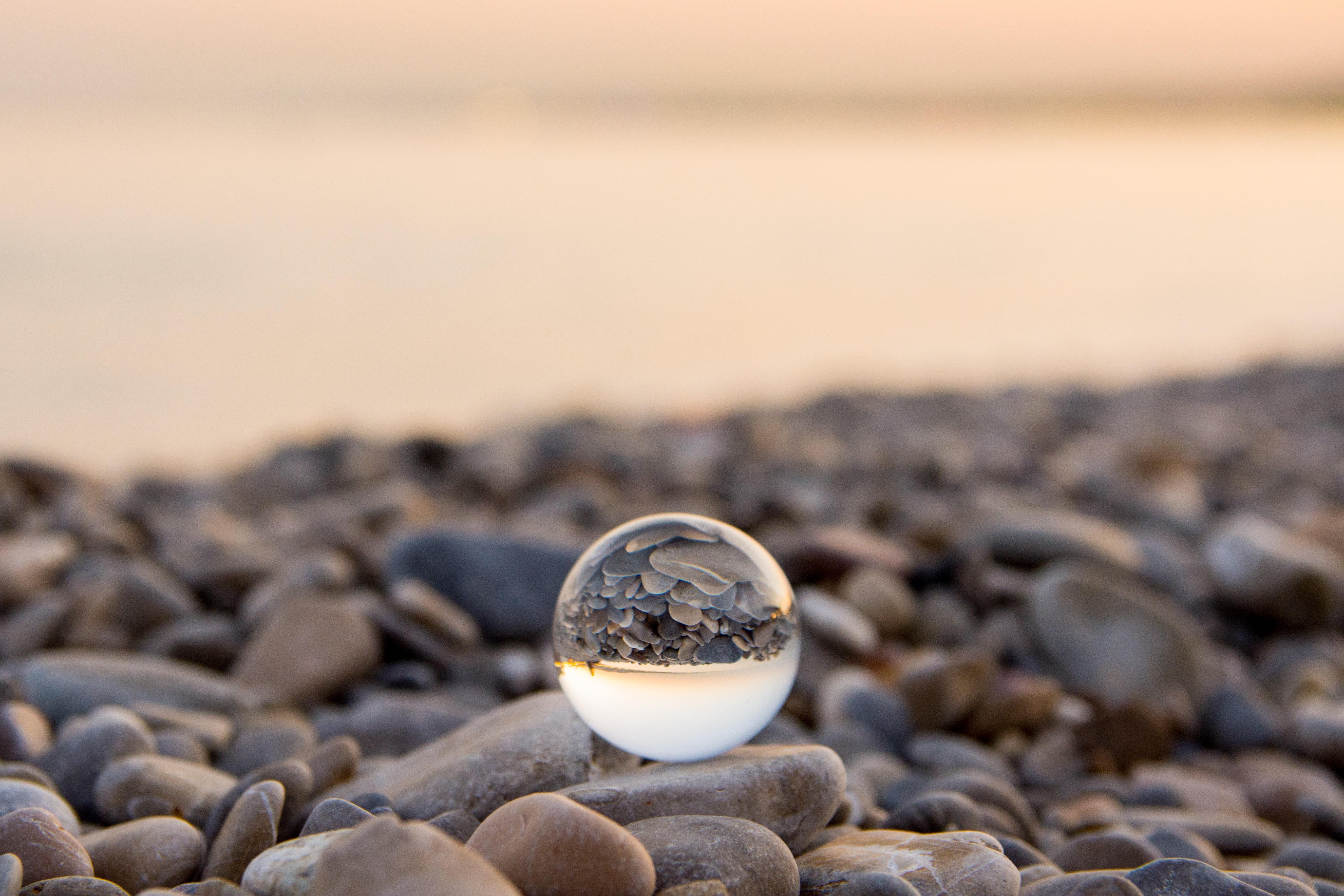 a photograph of a glass sphere on a pebbly beach
