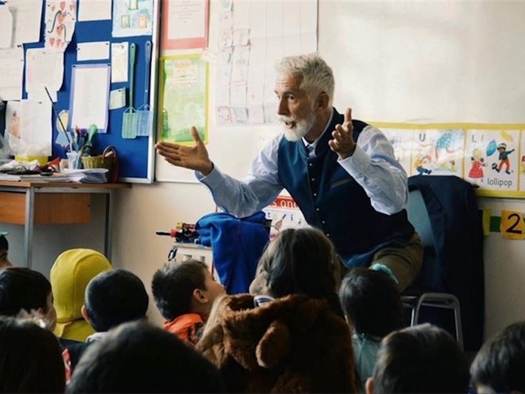 Sef Townsend, a man with white hair and beard tells stories to a group of young people sitting on the floor