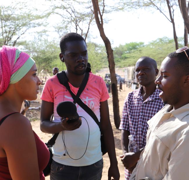 From Left: Storytellers Mara Menzies and John Namai interview Obed Tuyumvire, an entrepreneur (right) at the Lokiriama Peace Accord Commemoration in Lokiriama village, Turkana County, Kenya. Looking on is Turkana County Meteorological Services Director Francis Muinda.