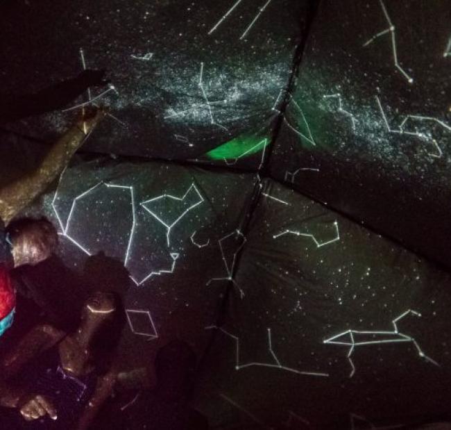 a small group of people look up at indoor projections of the constellations