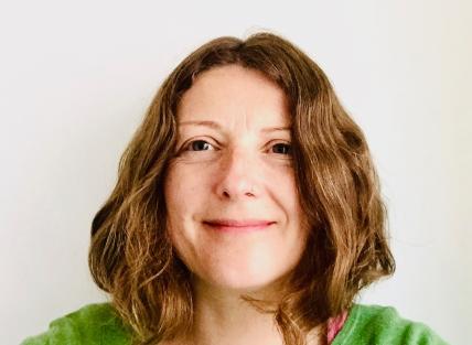 A woman with shoulder length light brown hair, wearing a green jumper