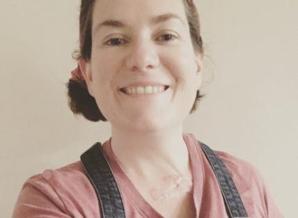 a white woman with dark hair, wearing a pink top and dungarees