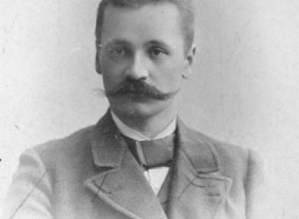 an old black and white photograph of I. K. Inha, a white man with a large moustache and short hair wearing formal clothing