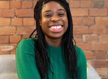 a young black woman with long dark hair and wearing a green jumper