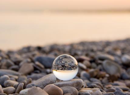 a photograph of a glass sphere on a pebbly beach